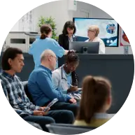 A busy reception area with people seated, while staff assist at the front desk and interact with patients.
